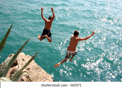 Two boys jumping into water from a rock