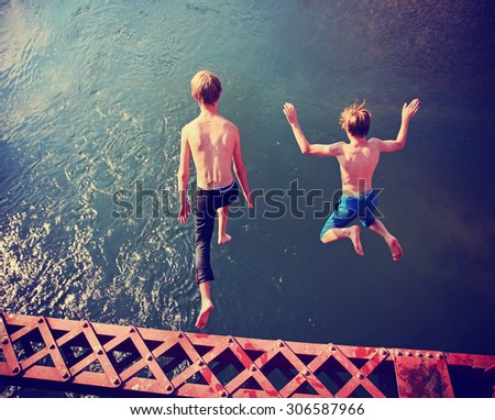  two boys jumping of an old train trestle bridge into a river toned with a retro vintage instagram filter effect app or action
