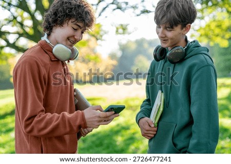 Two boys looking at a phone while standing in a park during daytime in autumn
