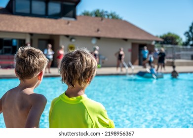 Two Boys Looking Towards A Cardboard Boat Floating In A Pool.