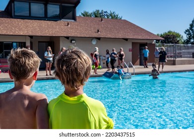 Two Boys Looking Towards A Cardboard Boat Floating In A Pool.