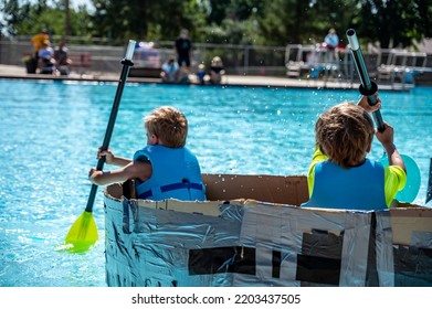 Two Boys Paddling A Cardboard Boat In A Race In A Pool