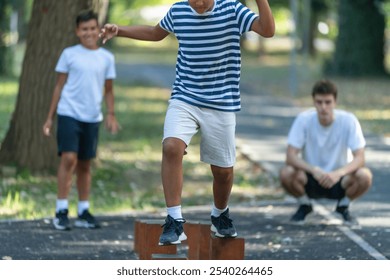 Two boys participate in outdoor sports activities, balancing across wooden stumps under the guidance of a trainer. The natural setting fosters coordination and focus during this playful exercise. - Powered by Shutterstock