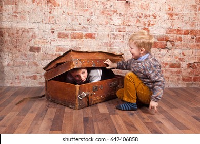 Two boys play hide and seek in the old vintage suitcase on the brick wall background