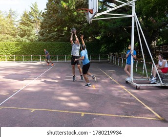 Two Boys Playing Basketball And One Playing Football On An Outdoor Basketball Court And Two Girls Watching Them Wearing Masks In Time Of Covid19