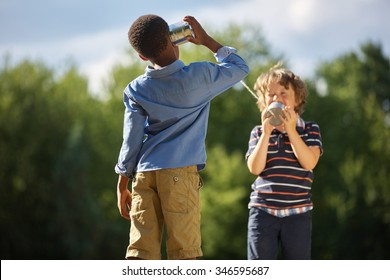 Two boys playing tin can telephone and having fun at the park