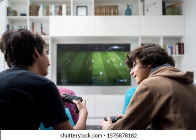 Two Boys Sitting At Home Playing Video Games On Game Console