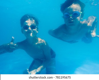 Two Boys Swimming Under Water With Thumbs Up In The Pool 