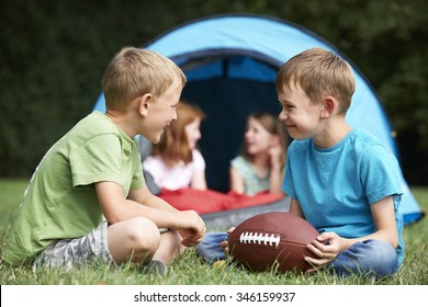 Two Boys Talking And Playing With American Football On Camping T