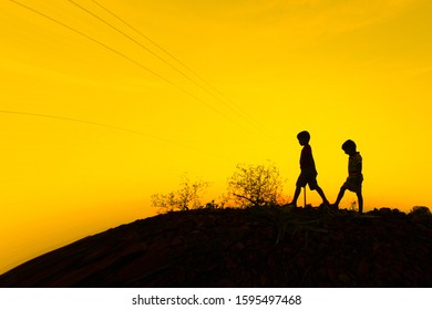 Two boys walking down the hill during sunset to their homes after playing