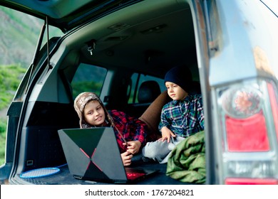 Two Boys Watching A Video On A Laptop In The Trunk Of A Car