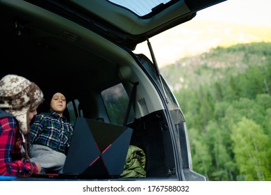 Two Boys Watching A Video On A Laptop In The Trunk Of A Car