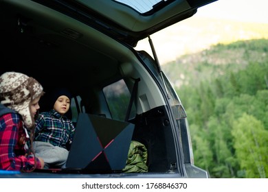 Two Boys Watching A Video On A Laptop In The Trunk Of A Car