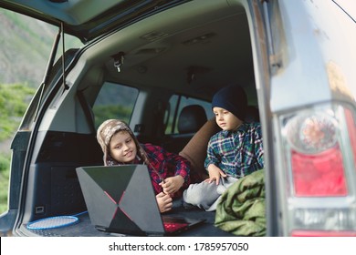 Two Boys Watching A Video On A Laptop In The Trunk Of A Car