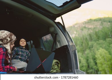 Two Boys Watching A Video On A Laptop In The Trunk Of A Car