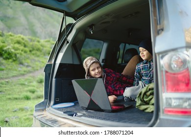 Two Boys Watching A Video On A Laptop In The Trunk Of A Car