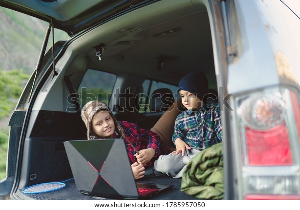 two boys watching a video on a laptop in the trunk of\
a car