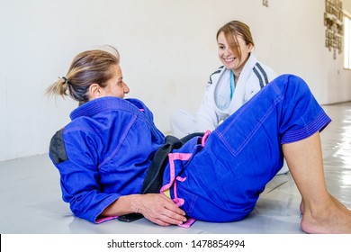 Two brazilian jiu jitsu bjj judo female judoka fighters women sitting and talking to each other during the brake in the training on the mats wearing kimono gi - Powered by Shutterstock