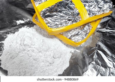 Two Bricks Of Cocaine Wrapped In Foil Beside A Heap Of Cocaine.