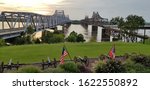 Two bridges crossing the Mississippi River contrasting old and new, railroad and highway, and train and road in Vicksburg, Mississippi with the United States and State of Mississippi flag flying.