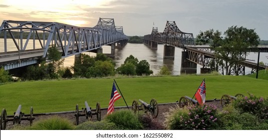 Two bridges crossing the Mississippi River contrasting old and new, railroad and highway, and train and road in Vicksburg, Mississippi with the United States and State of Mississippi flag flying.
