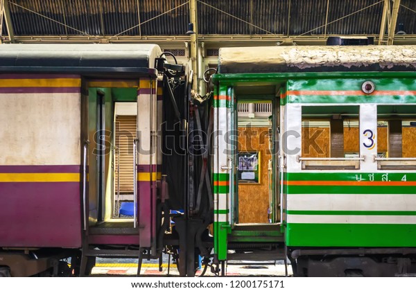 Two bright, colorful train\
train cars at the terminal station. Side view. Violet and green\
coach connection with open doors and tambours. Railway\
romance.