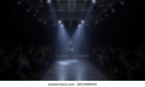 Two bright spotlights shine down on an empty stage, creating a dramatic atmosphere. The audience is blurred in the background, suggesting anticipation.
