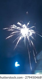 Two bright white fireworks exploding in a dark blue night sky, one dense like a sparkler, the other daisy-shaped with light trails, surrounded by smoke.