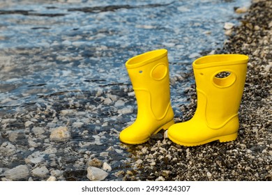 Two bright yellow children's rubber boots (gumboot) stand on the rocks at the water's edge.
 - Powered by Shutterstock