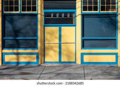 Two bright yellow doors with chrome handle to a store with blue trim. Over the door is a transom glass window with multiple panes. There's a sidewalk in front of the tall entrance to the vintage shop  - Shutterstock ID 2188342685