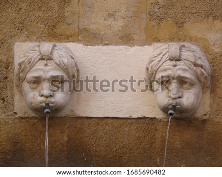 Two brother statues fontain with curious faces spit water in the roman area of Aix en provence