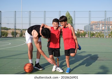 Two brothers helping to their sibling with a leg prosthesis to stretch his other leg. Siblings stretching before playing basketball.