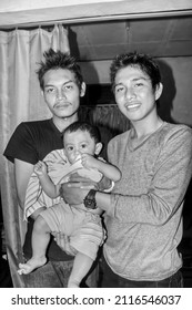 Two Brothers Are Holding The Little Boy And Smiling. Asian Family On House. Black And White Photography. Central Kalimantan, Indonesia. February 15, 2013. 