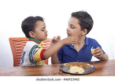 Two Brothers Sharing Their Food On Wooden Table And Young Boy Nagging For His Favourite Thing.