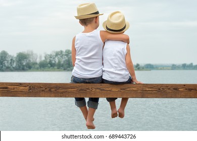 Two brothers in a straw hats sitting on the pier and looking at the lake.Summer vacation . - Powered by Shutterstock