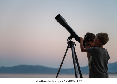 Two brothers, toddler boys, looking at the stars using a telescope by the sea on a beautiful summer night.