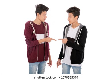 Two brothers twins pointing with fingers at each other with serious faces, isolated on a white background.