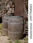 Two brown antique wooden barrels against brown door and stone wall. Harper