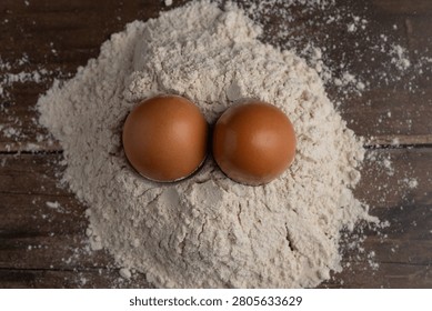 Two brown eggs rest together in a soft nest of scattered flour on a rustic wooden surface, evoking themes of baking and food preparation.