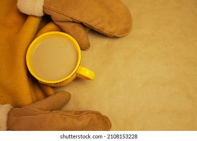 Two Brown Mittens, Orange Scarf, Yellow Mug, Beige Background