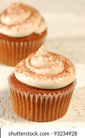 Two Brown Pumpkin Spice Cupcakes With Butter Cream Frosting Sprinkled With Cinnamon Powder, With Selective Focus On The Cupcake In The Foreground.