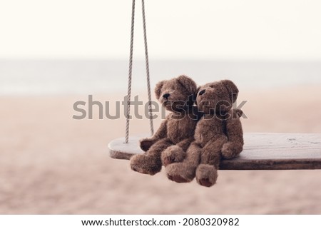Two brown teddy bears so cute sitting on wooden swing looking to the sea in romantic moment. Concept of love and valentine's day or wedding, Cinematic tone.