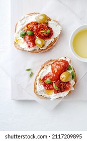 Two bruschettas with ricotta cheese, olive and dried tomatoes on ciabatta bread on white background. Olive oil and spices decorated. Copyspace. - Shutterstock ID 2117209895