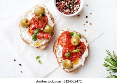 Two bruschettas with ricotta cheese, olive and dried tomatoes on ciabatta bread on white background. Olive oil and spices decorated. Copyspace. - Shutterstock ID 2124682472