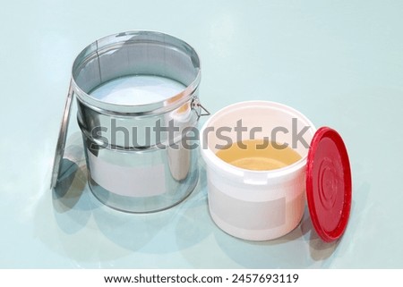Two buckets with open caps, containing epoxy resin for flooring. Two buckets of chemical materials, one of them is metal and the other one is made of plastic.
