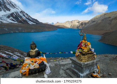 Two Buddha statues at the Tilicho Lake, covered with prayer flags. Blue and calm surface of the lake, mountains covered in the shadow, sunlight in the back. Annapurna Circuit Trek, Nepal. Spirituality