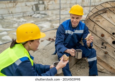 Two Builders In Hardhats And Workwear Having Sandwiches With Tea At Lunch Break