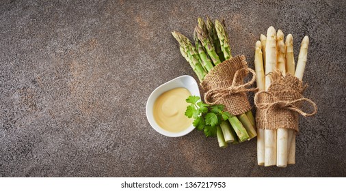 Two bundles of fresh raw green and white asparagus tied with hessian on a textured grey stone background with copy space in banner format