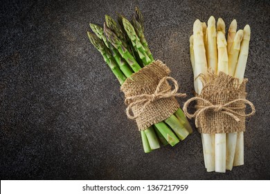 Two bundles of fresh white and green spring asparagus tied with hessian and string on a textured grey background with copy space