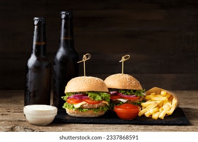 Two burgers, french fries, beer in dark bottles on a wooden background. Fast food, homemade hamburgers - Powered by Shutterstock